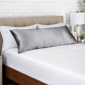 Gray satin pillow on a bed with white bedding and a wooden headboard.
