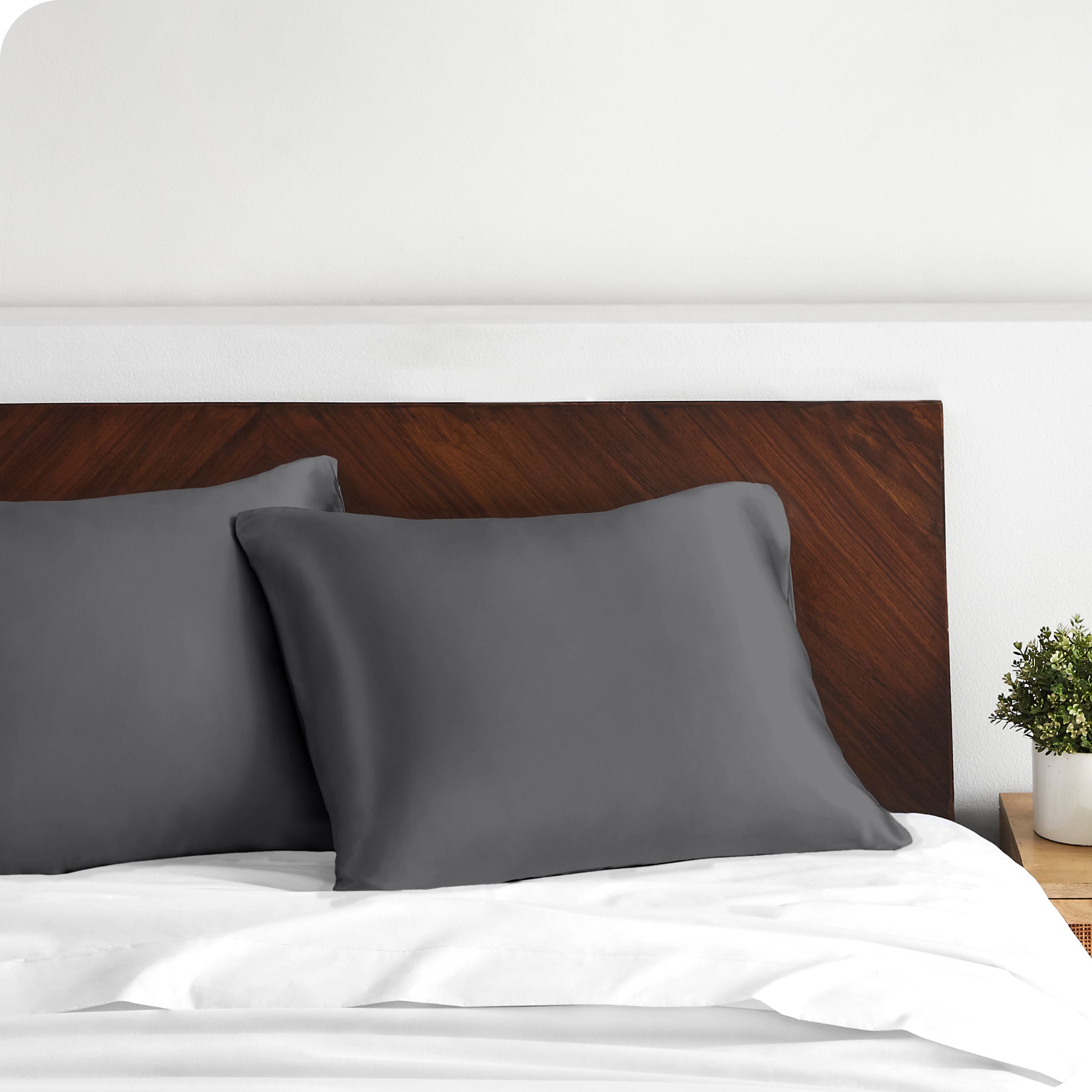 Two satin pillowcases on pillows against a wooden headboard