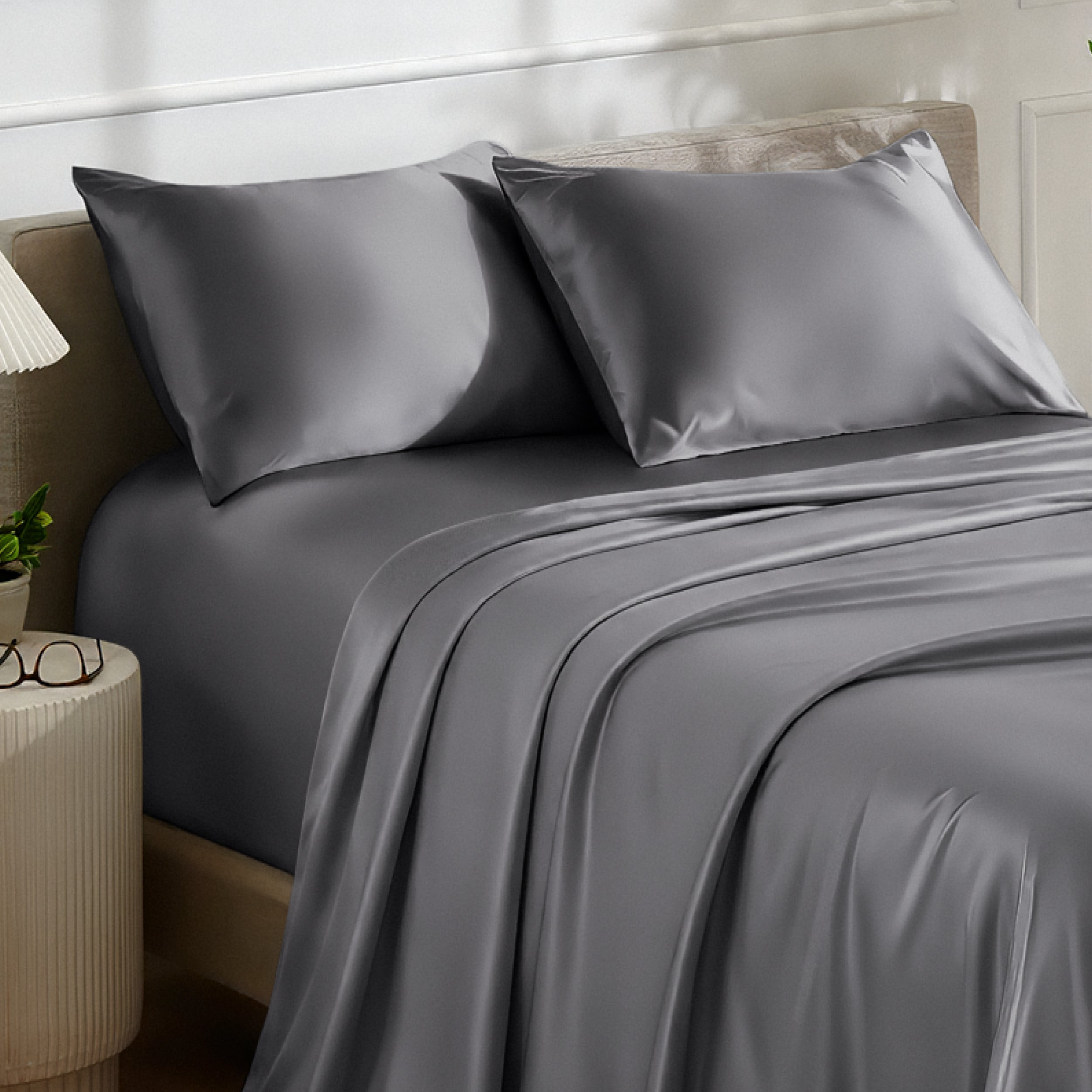 Satin bedding set on a bed with a nightstand and lamp in the background.
