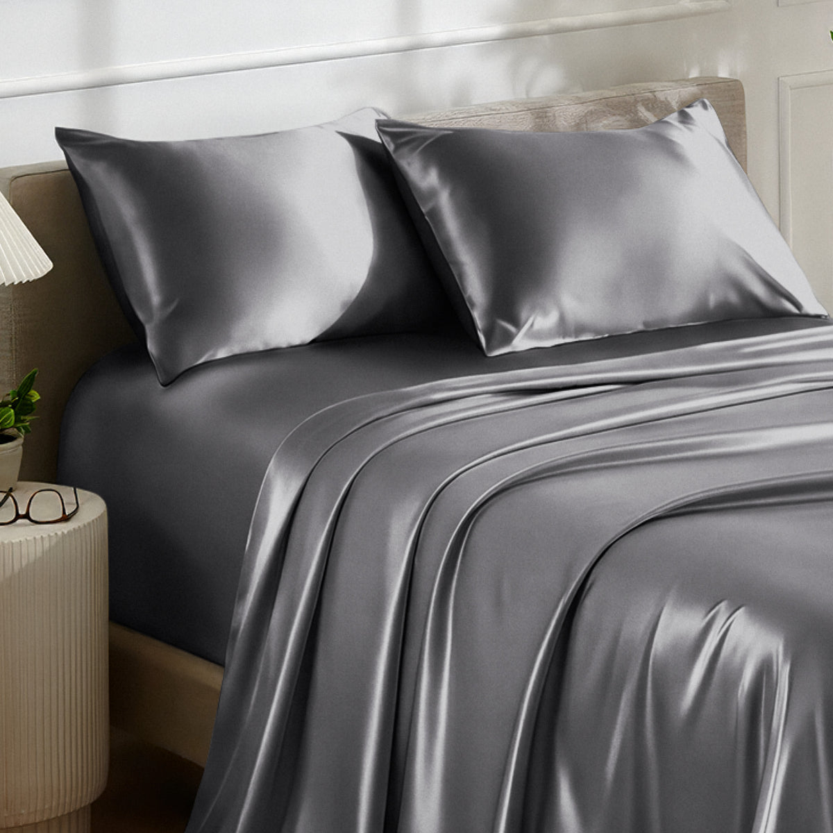 Satin bedding set on a bed with a nightstand and lamp in the background.