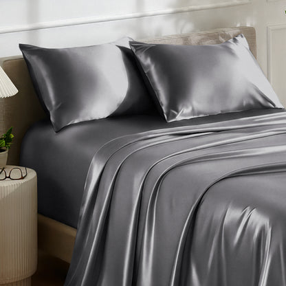 Satin bedding set on a bed with a nightstand and lamp in the background.