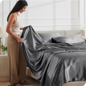 A woman is putting satin sheets on a bed