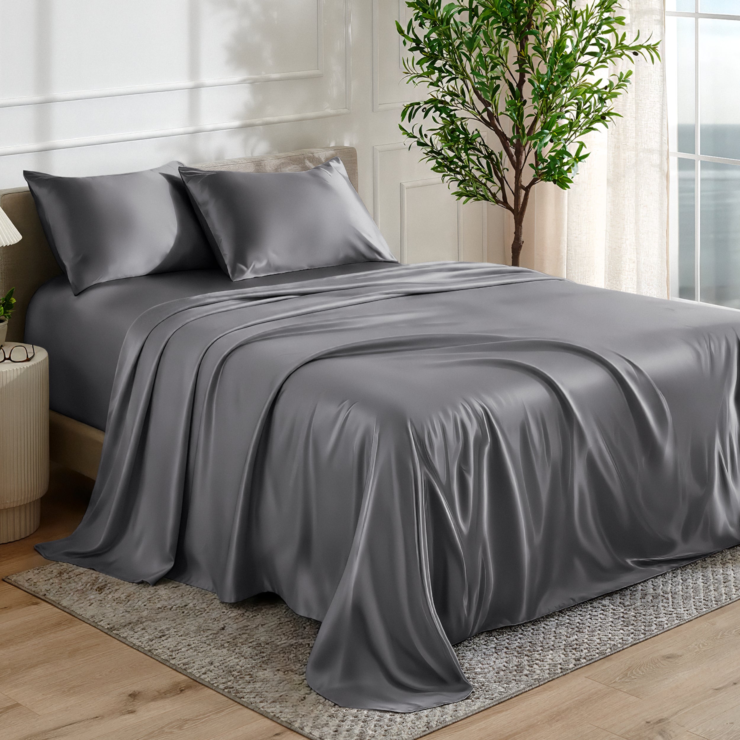 Satin sheet set on a bed in a bedroom with a plant and window in the background.