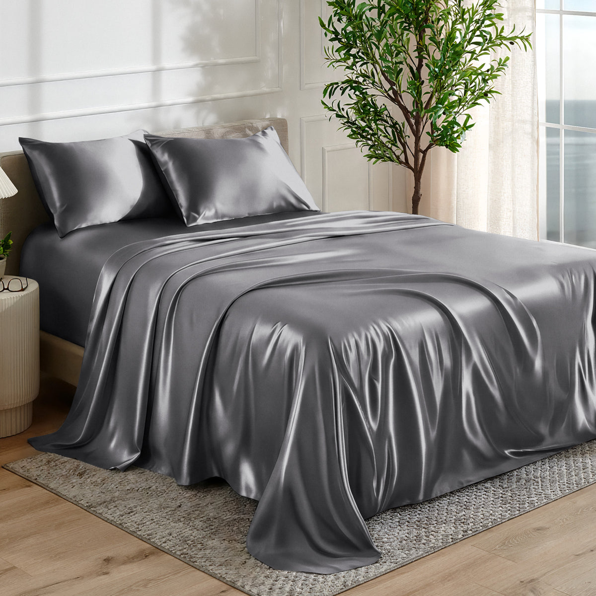 Satin sheet set on a bed in a bedroom with a plant and window in the background.