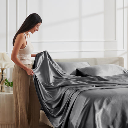 Woman arranging satin bedding on a bed in a bright bedroom.