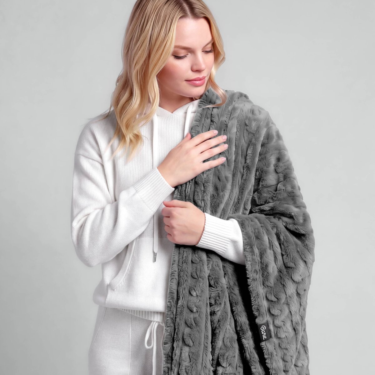A woman is standing with a textured faux shearling blanket over her shoulder