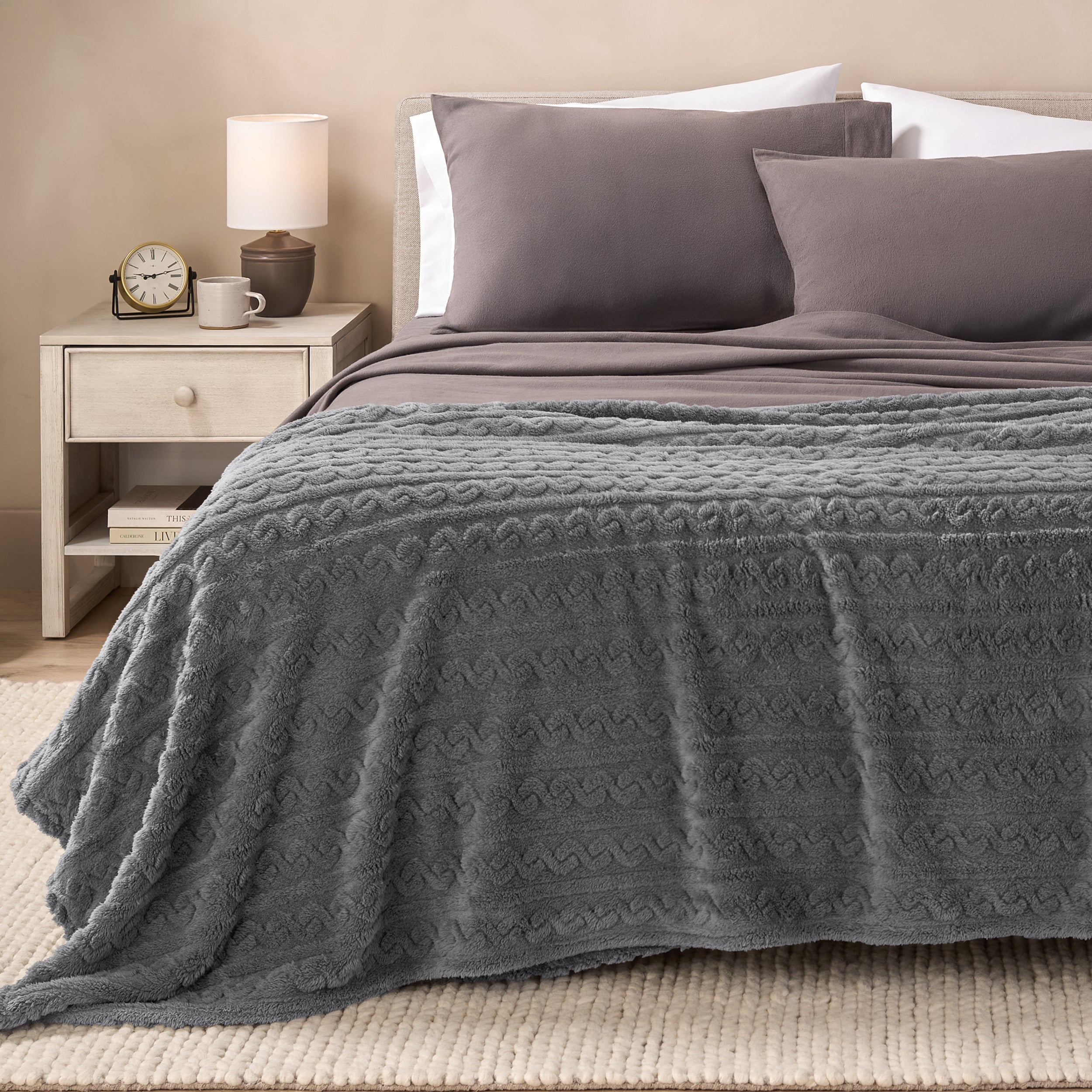 A textured sherpa blanket draped over the end and side of a bed