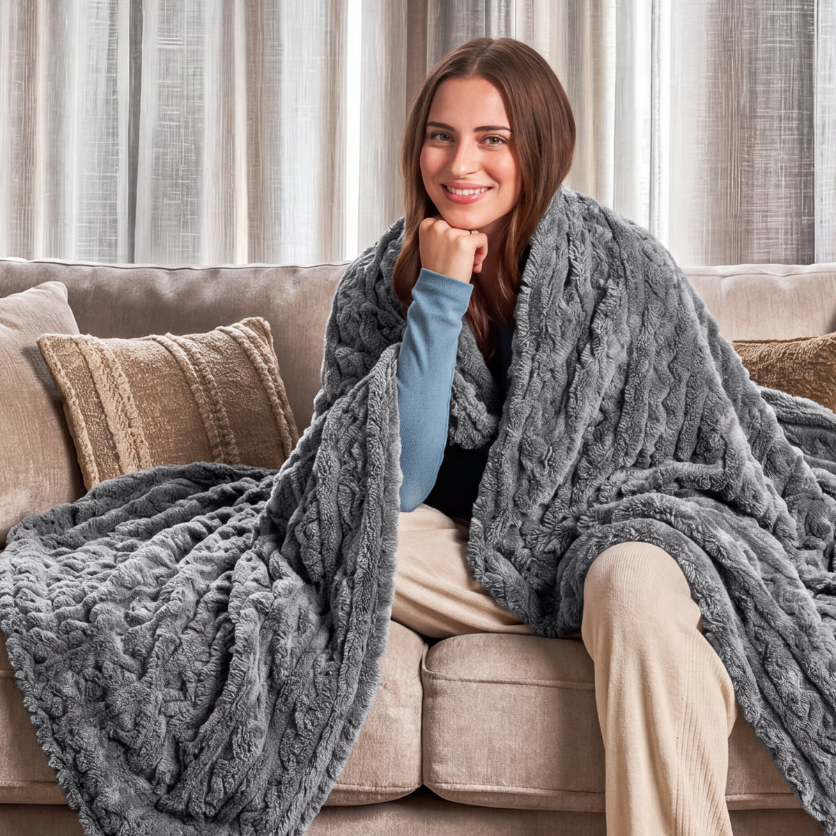 Woman sitting on a couch wrapped in a grey blanket in a cozy living room.