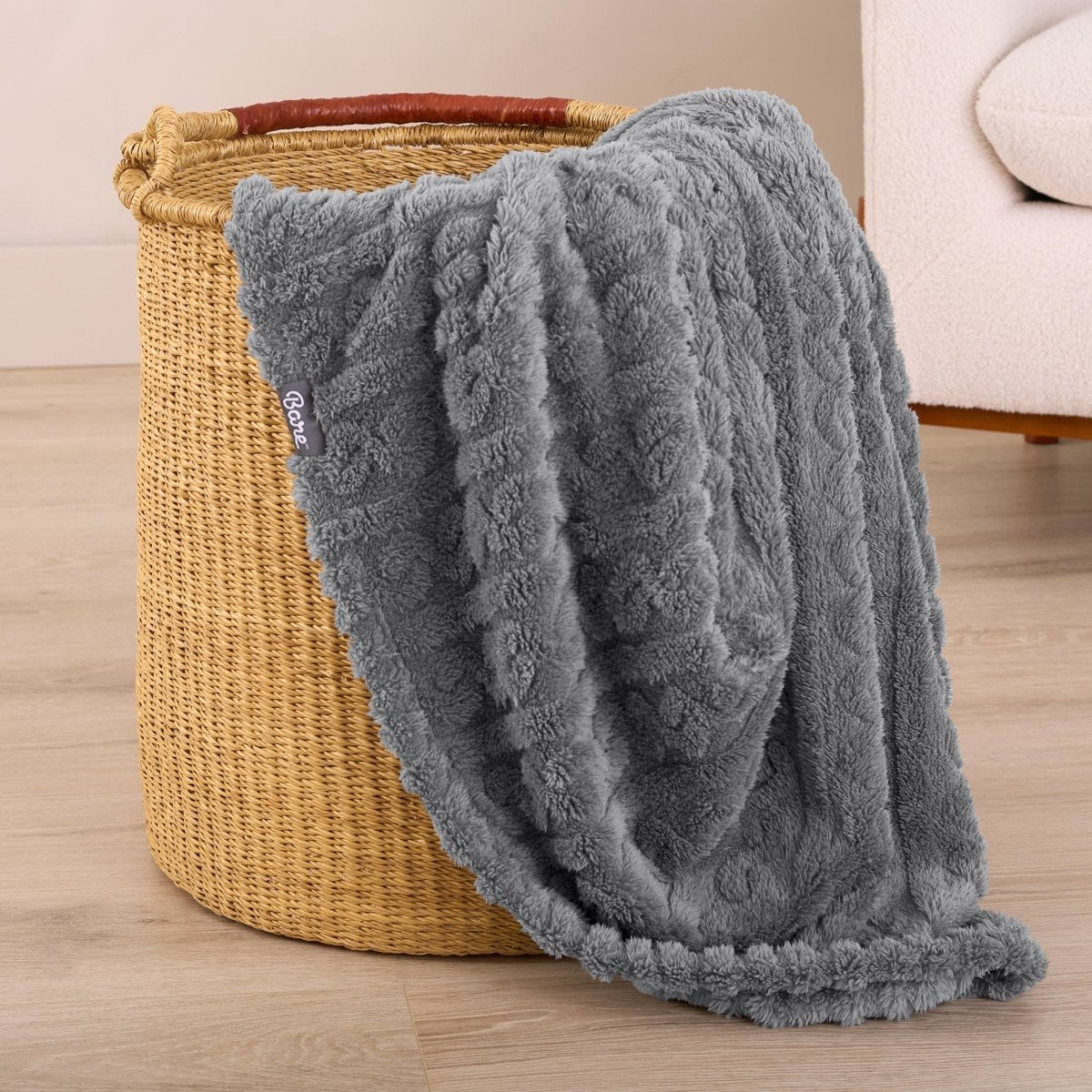 Gray textured blanket draped over a woven basket on a wooden floor.