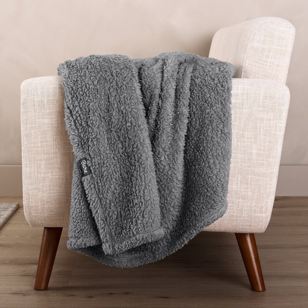 Faux shearling blanket draped over a beige armchair with a wooden base.