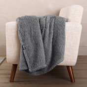 Faux shearling blanket draped over a beige armchair with a wooden base.