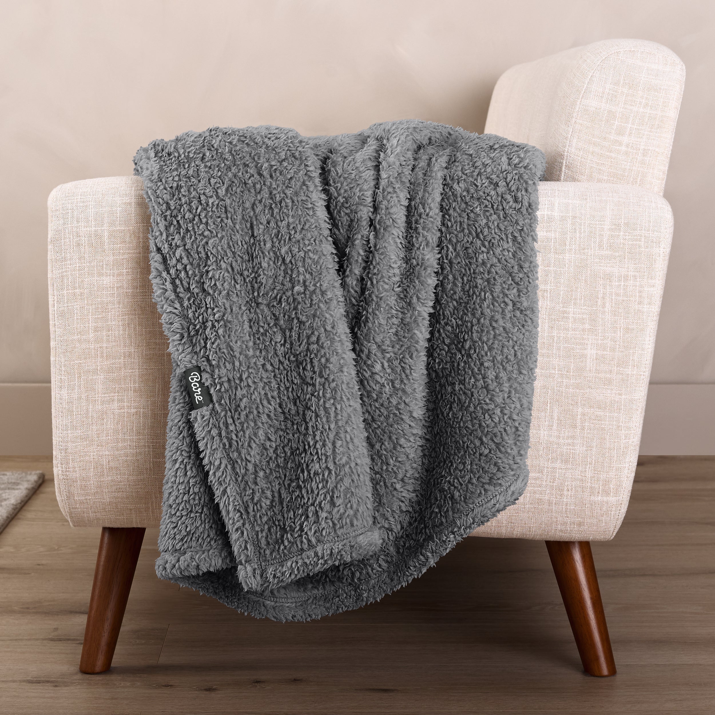 Faux shearling blanket draped over a beige armchair with a wooden base.