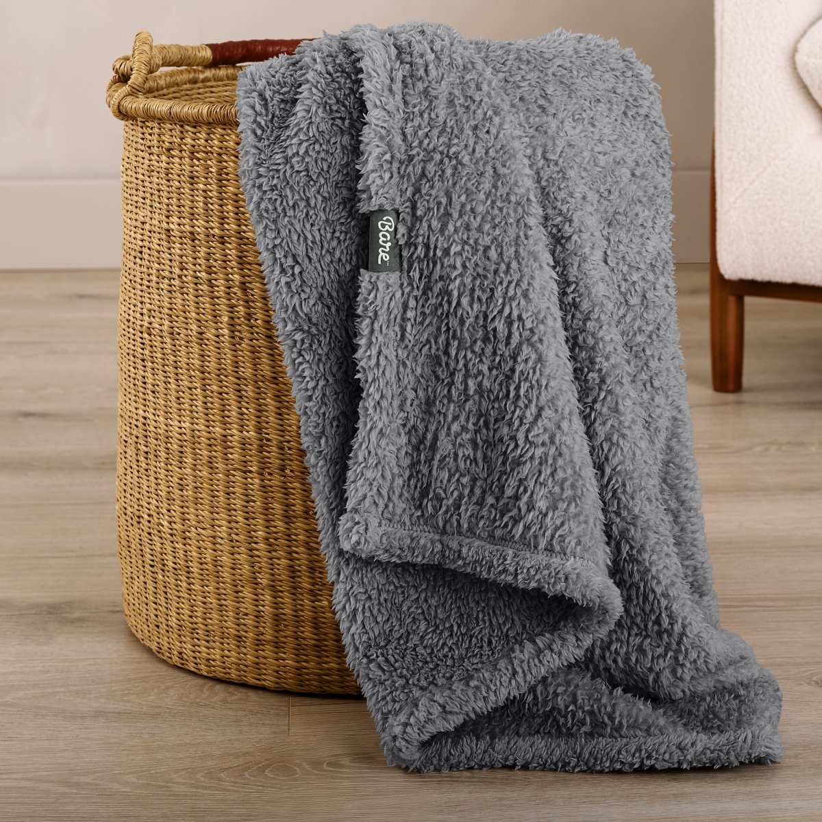 Fluffy blanket draped over a woven basket on a wooden floor.