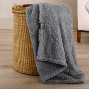 Fluffy blanket draped over a woven basket on a wooden floor.