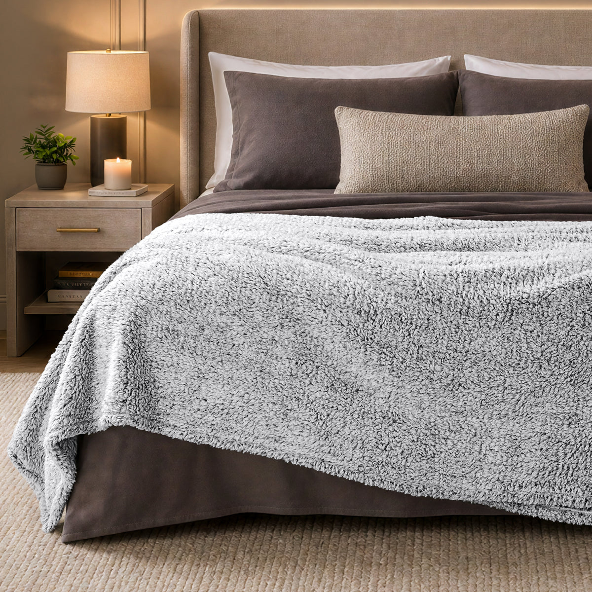 A bed with a tipped sherpa blanket draped over the end