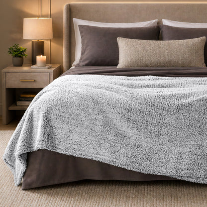 A bed with a tipped sherpa blanket draped over the end
