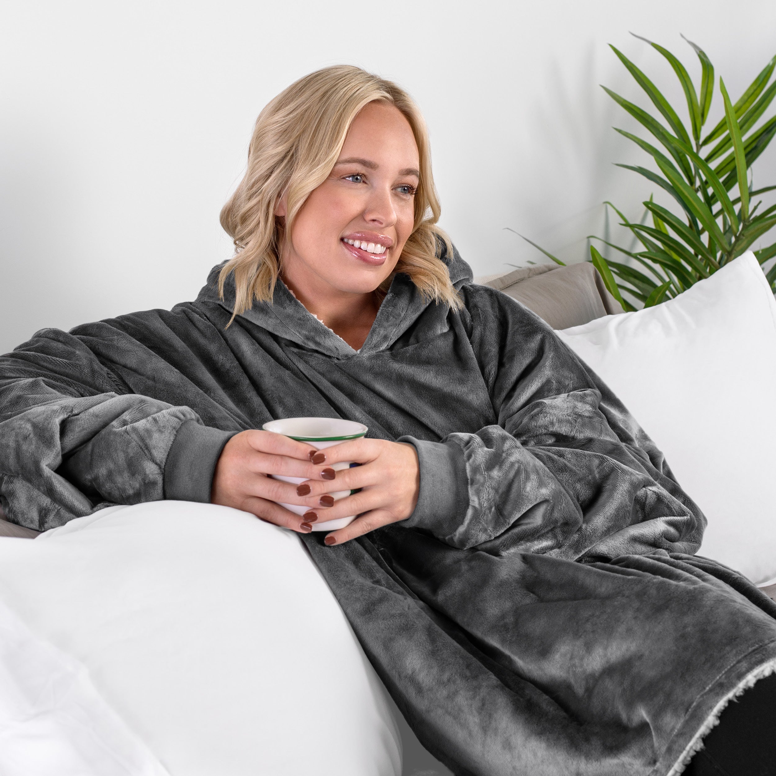 A woman sitting on a couch holding a mug wearing a sherpa blanket.