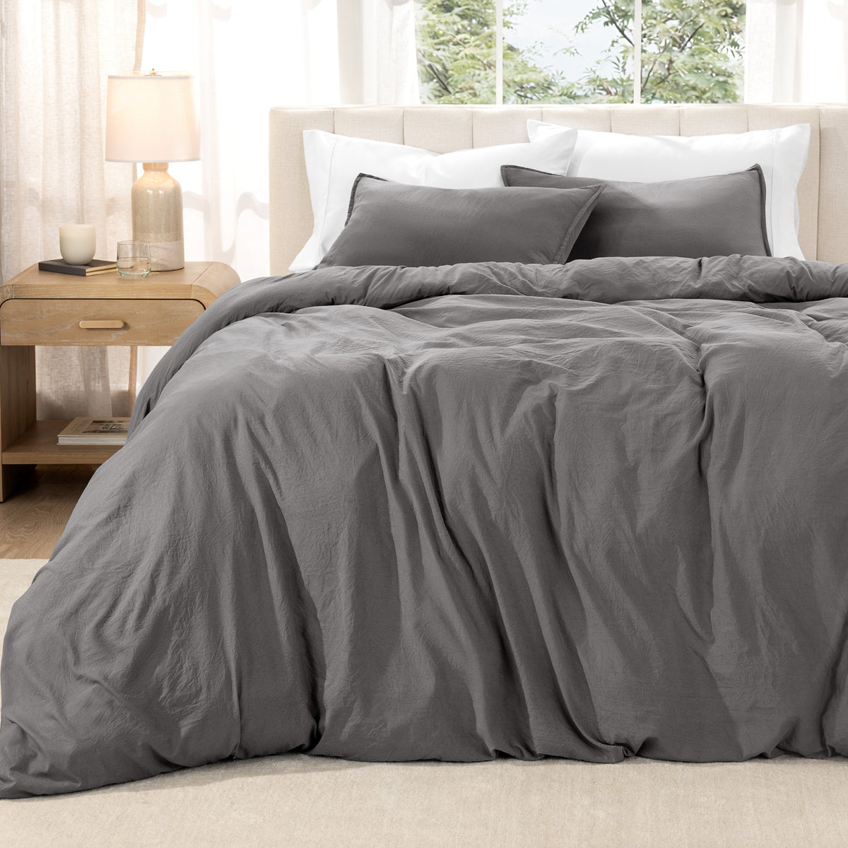 Washed duvet set on a bed in a bright bedroom with a lamp and window.
