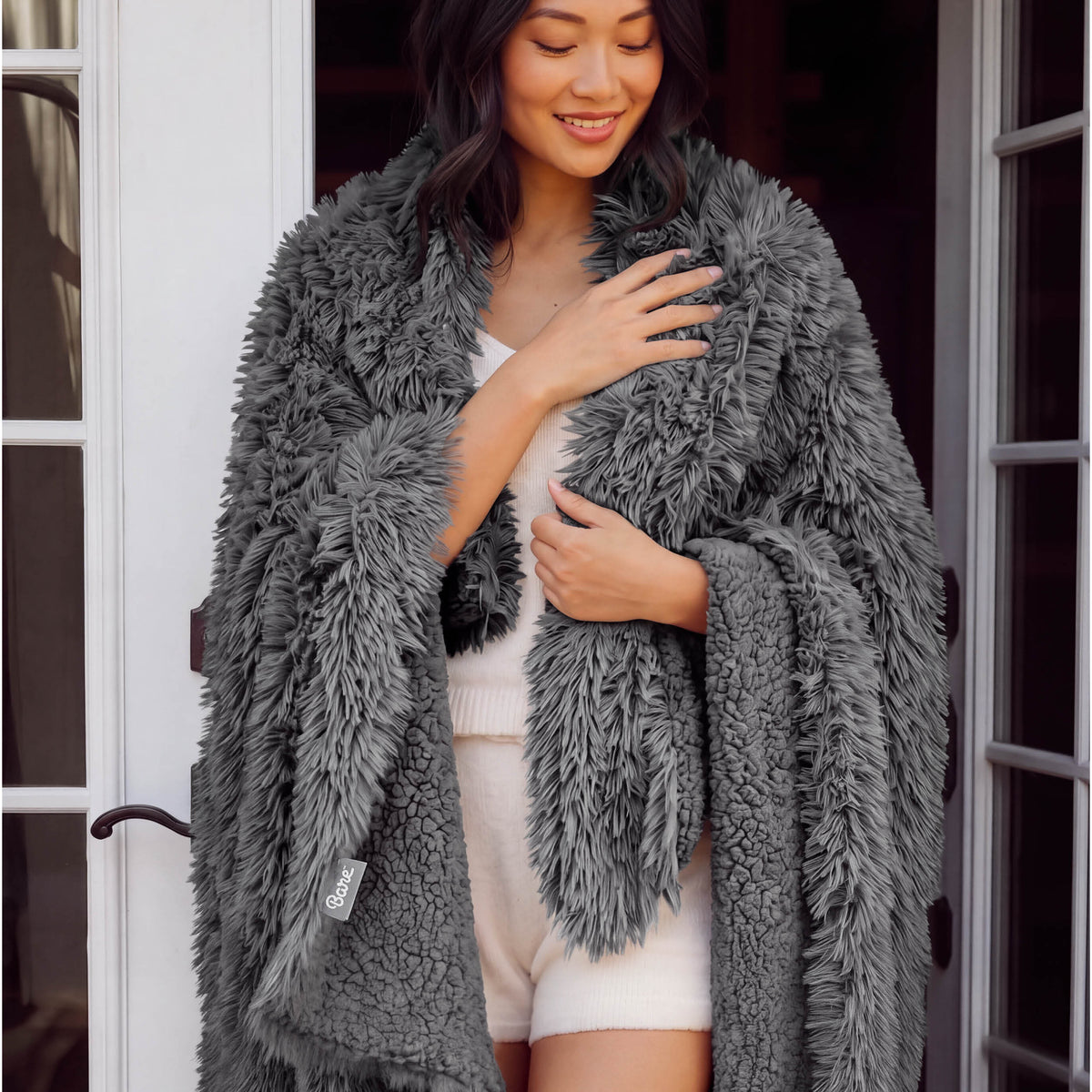 A woman standing with a shaggy blanket wrapped around her