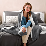 A woman sitting on a bed with a Sherpa blanket around her