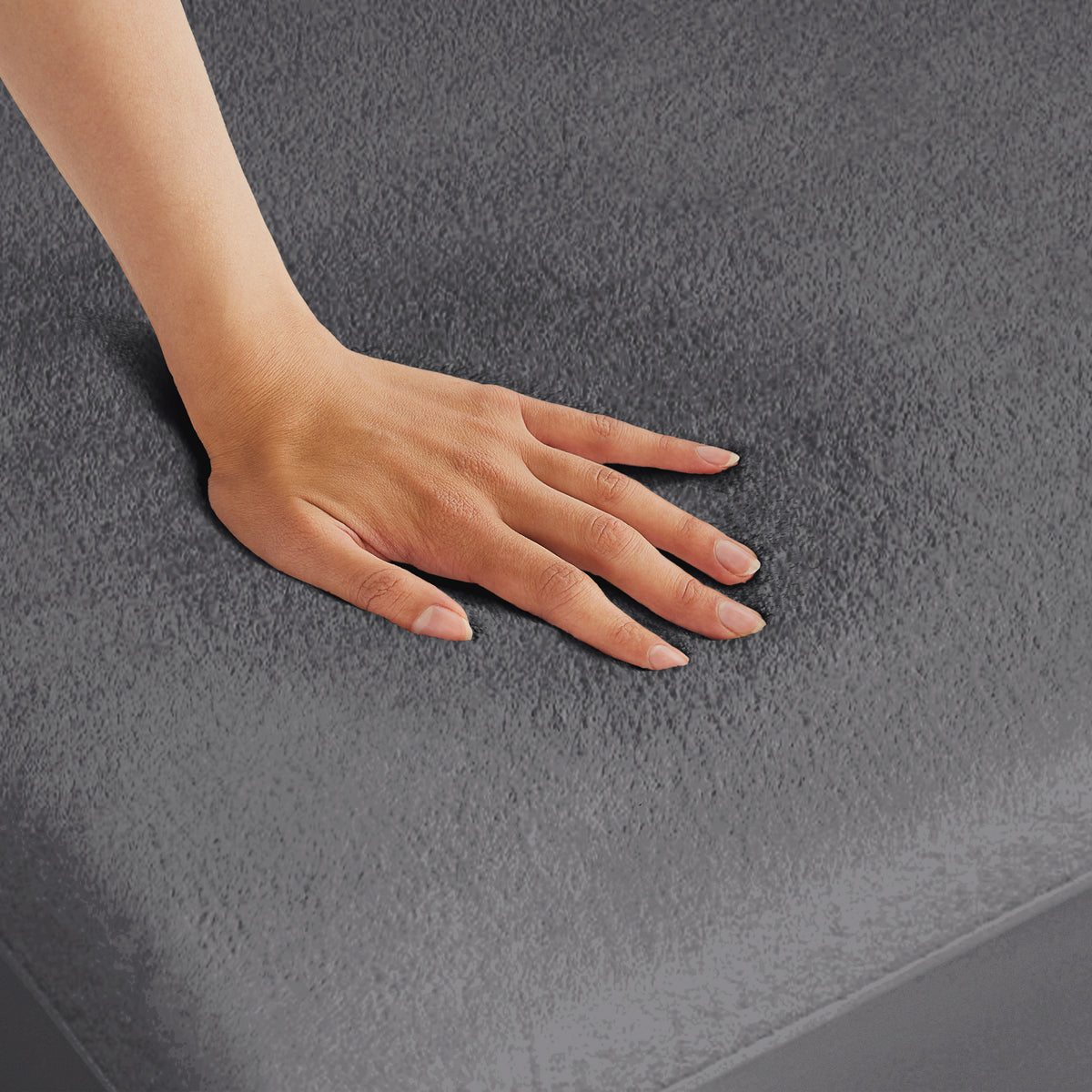A woman is pressing her hand down a mattress with a terry cotton mattress protector on it