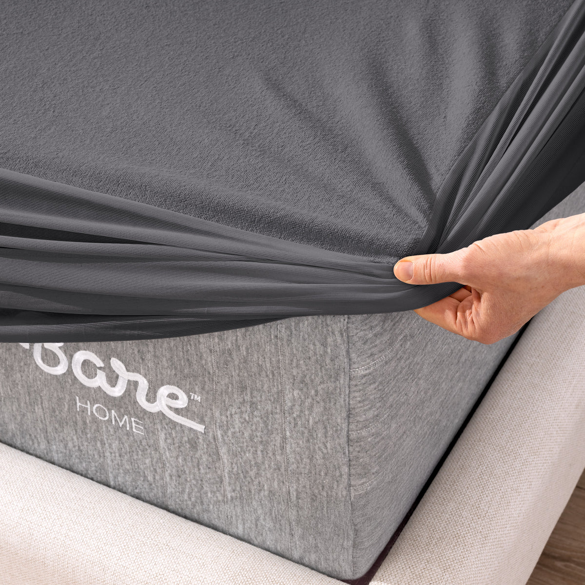 A person is pushing their hand down on a mattress covered with a mattress protector