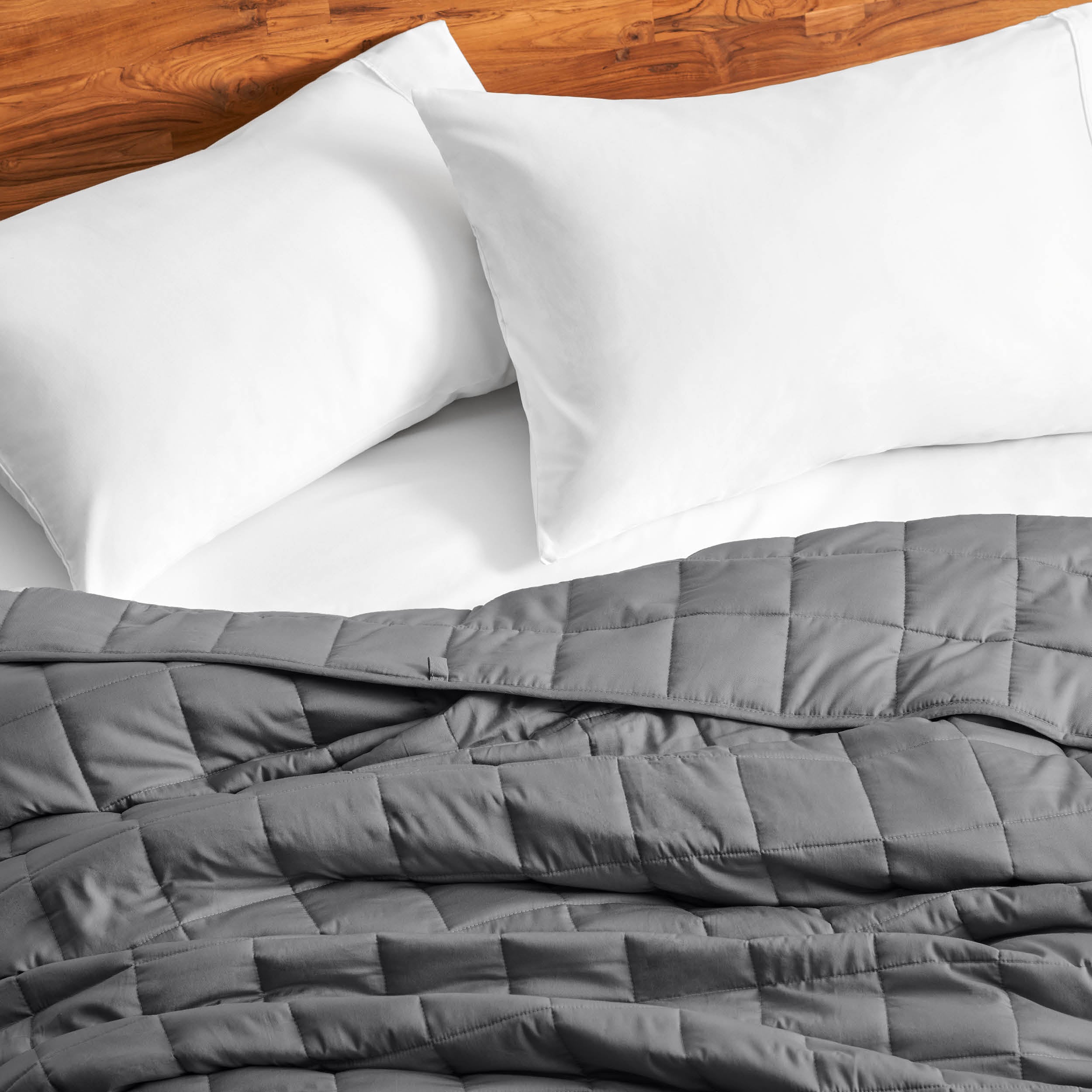 Cotton weighted blanket on a bed with white pillows against a wooden headboard.