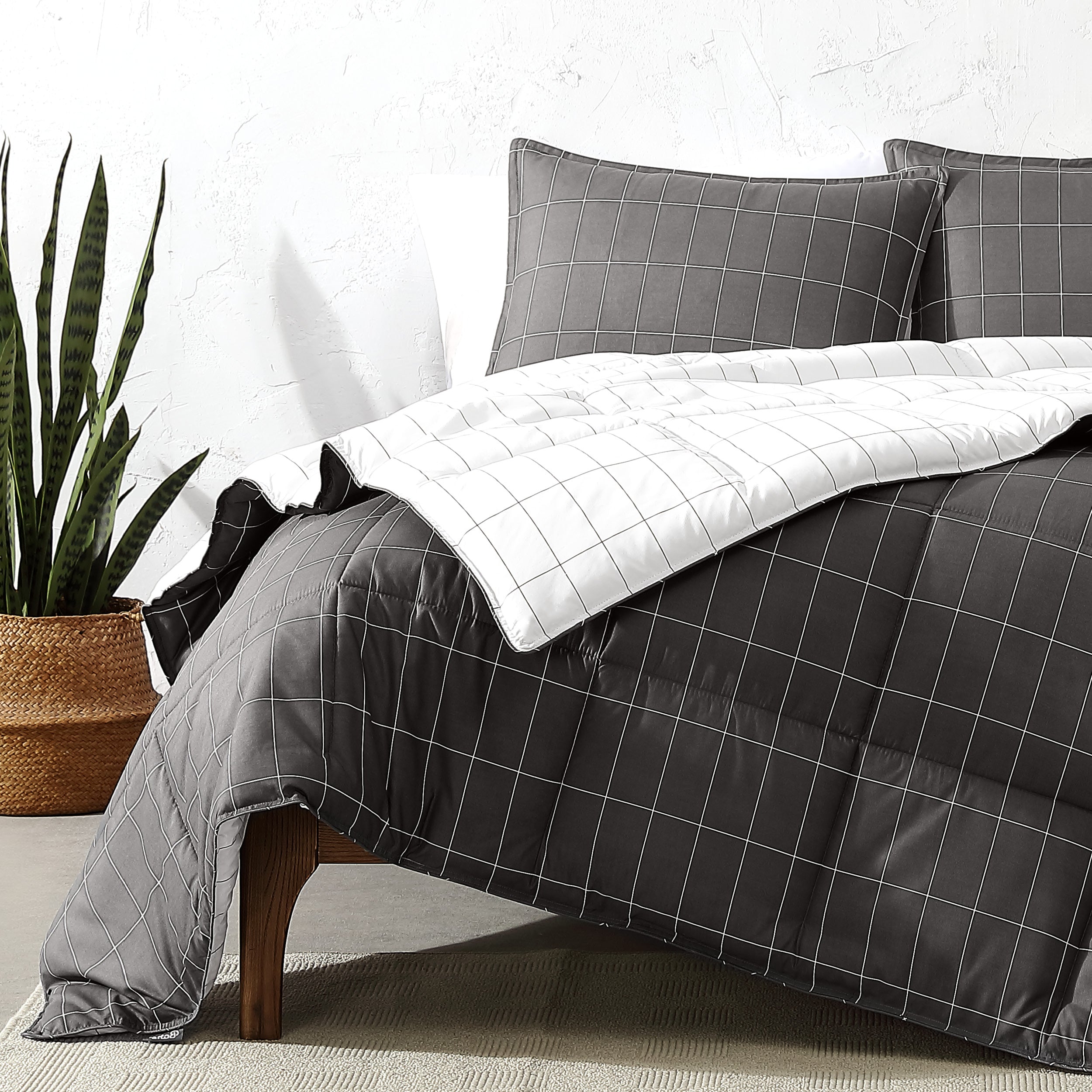 Gray grid-patterned comforter set on a bed with a plant in the background.
