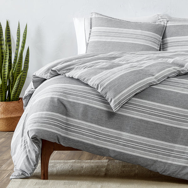 Gray striped bedding set on a bed with a plant in the corner.