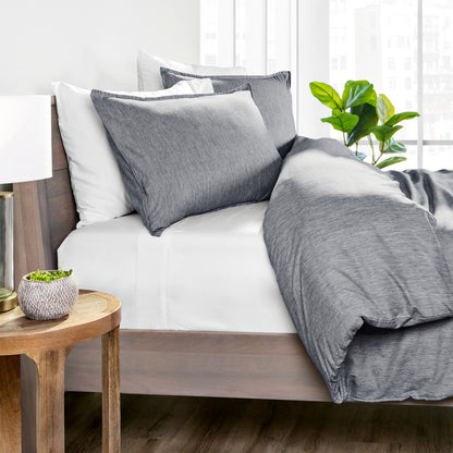 Gray bedding set on a bed with a wooden side table and plant in the background