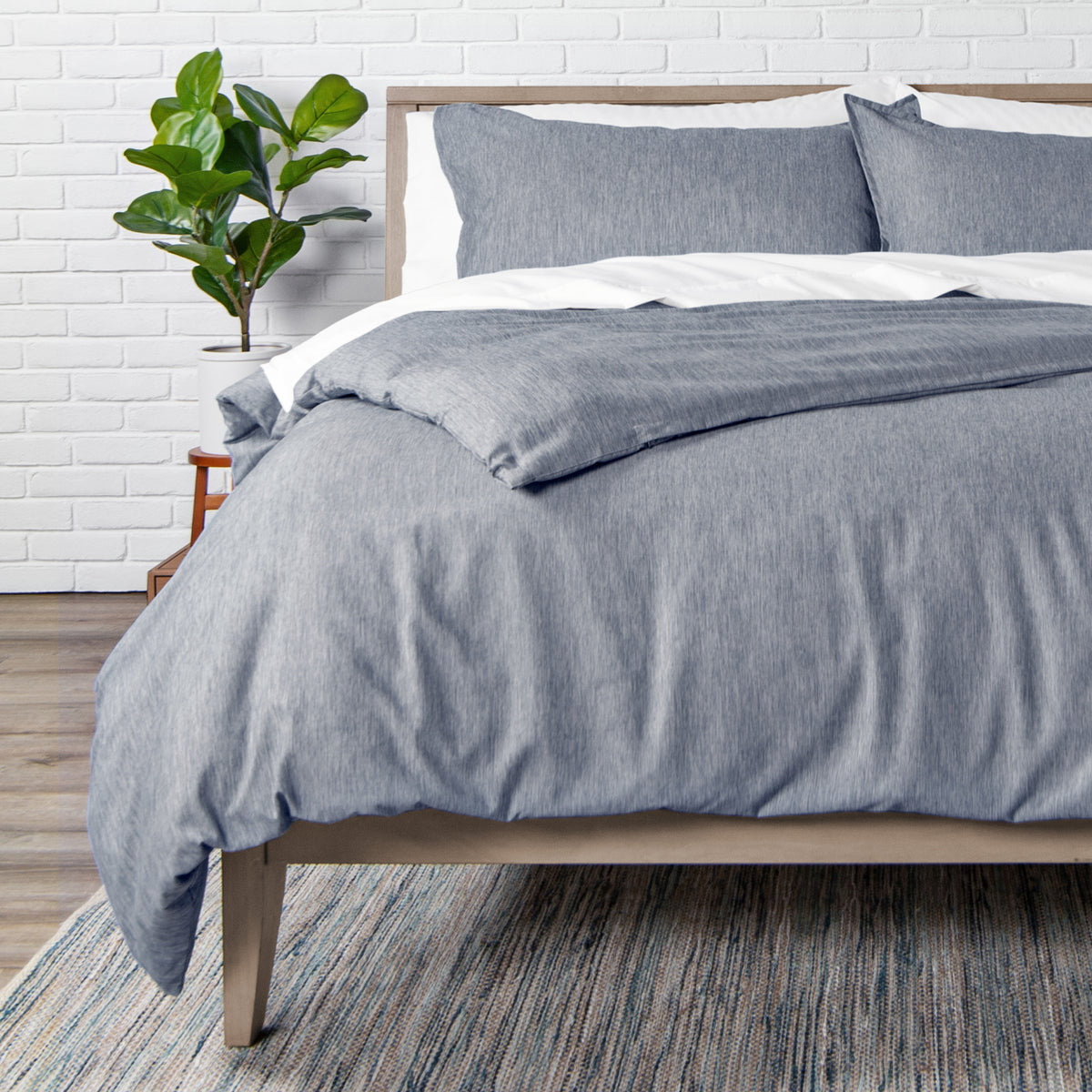 Bed with blue bedding and pillows against a white brick wall.