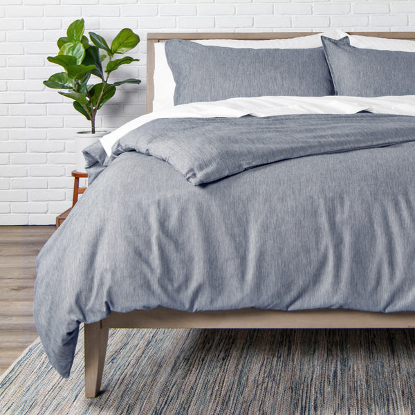 Bed with blue bedding and pillows against a white brick wall.