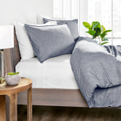 Blue bedding set on a bed with a wooden side table and plant in the background