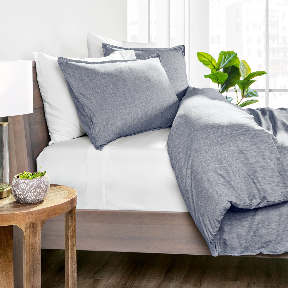 Blue bedding set on a bed with a wooden side table and plant in the background