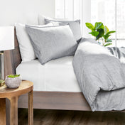 Gray bedding set on a bed with a wooden side table and plant in the background