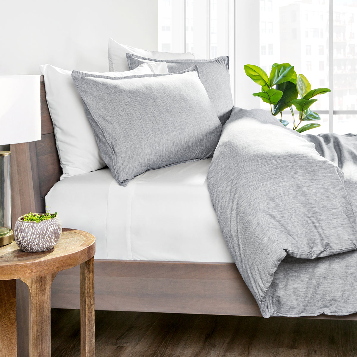 Gray bedding set on a bed with a wooden side table and plant in the background