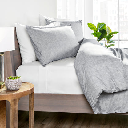 Gray bedding set on a bed with a wooden side table and plant in the background