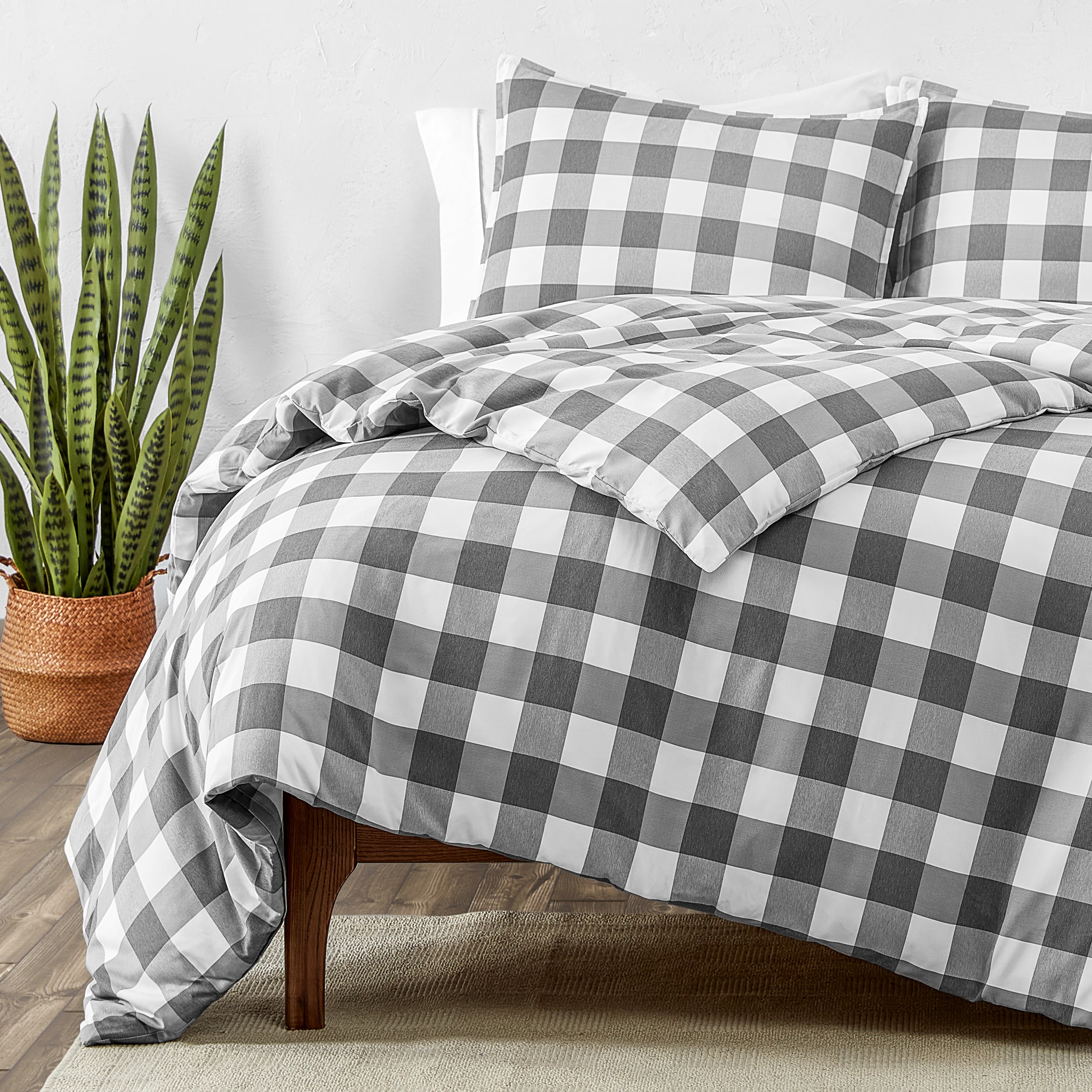 Bed with gray and white checkered bedding, accompanied by a potted plant.