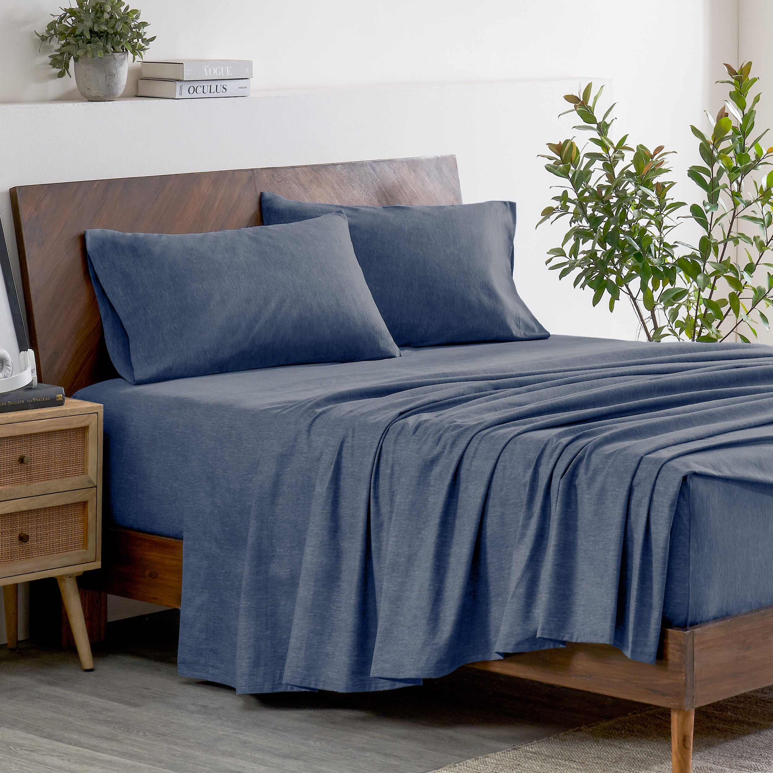 Indigo bedding set on a bed with a wooden headboard and plant in the background