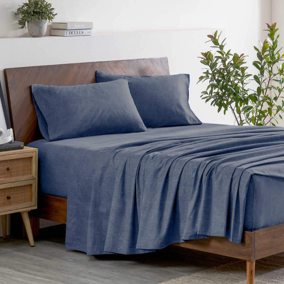 Indigo bedding set on a bed with a wooden headboard and plant in the background