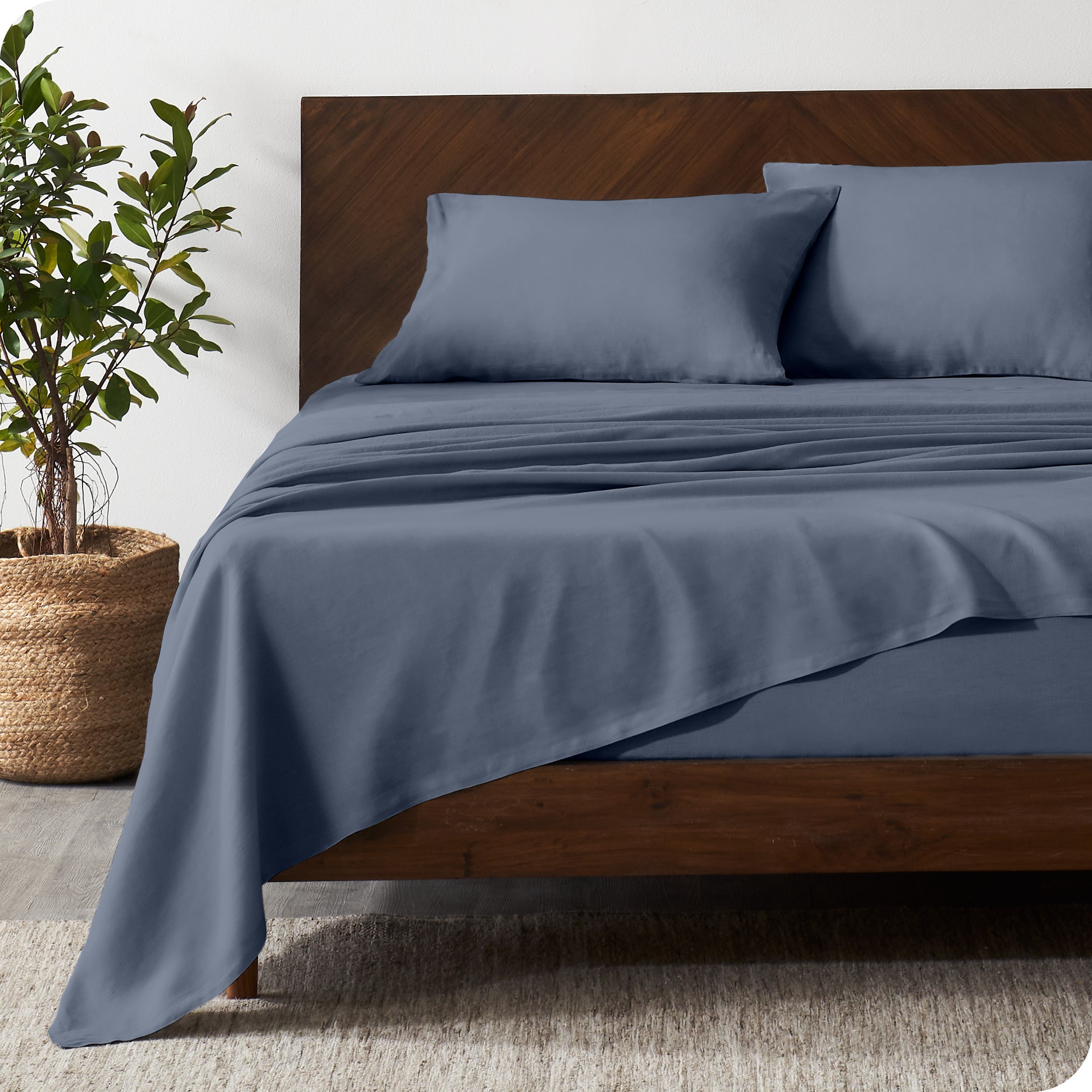 Dark wooden bed frame with indigo linen sheets on the mattress