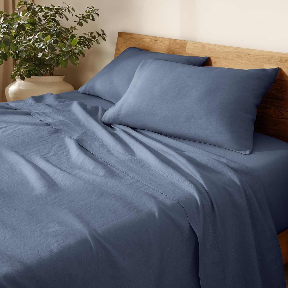 Linen bed sheets and pillowcases on a wooden bed with a plant in the background