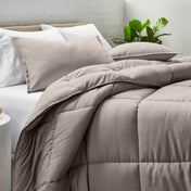 Comforter and pillow shams on a bed with a white brick wall and plant in the background