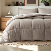 Comforter on a bed in a bedroom setting with a wooden nightstand and decorative items.