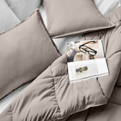 Comforter and pillows on a bed with a magazine and glasses.