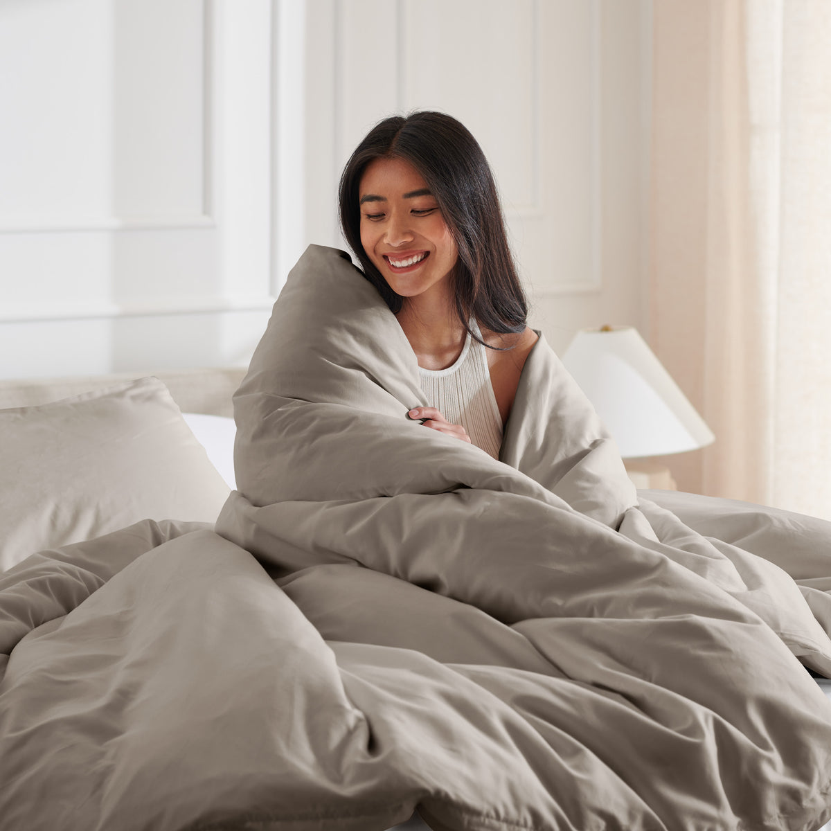 Woman smiling under duvet cover set in a bedroom setting