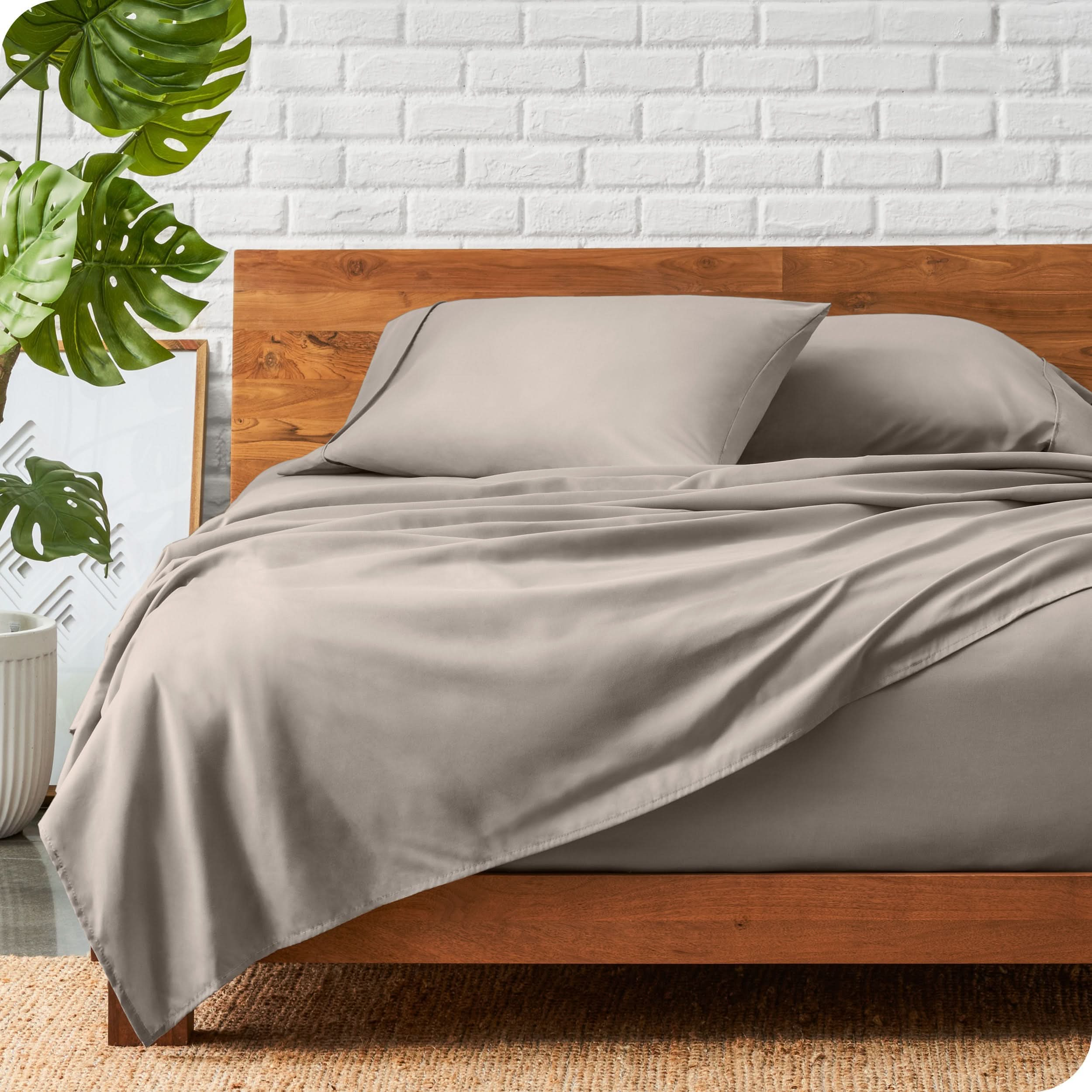 A wooden bed frame with a microfiber sheet set on the mattress.