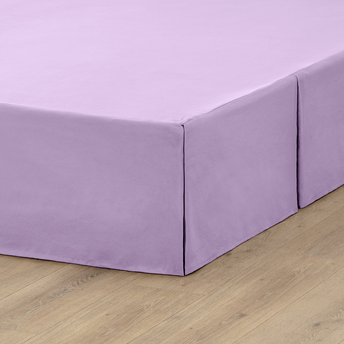 The corner of a box spring with a pleated bed skirt on it