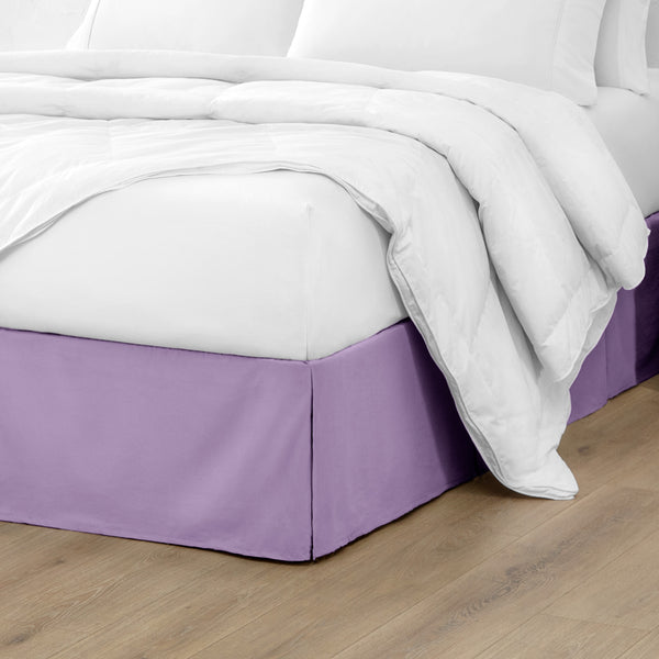 A modern bed with a microfiber bed skirt with pleats on the corners and midway on each side