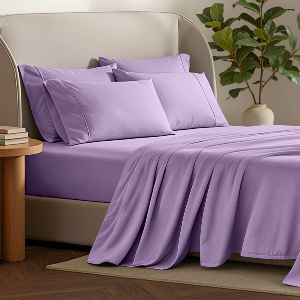 Bed sheets and pillows on a bed with a plant and side table in the background.